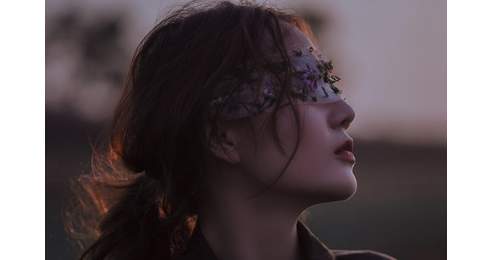 blindfolded woman in a field smelling the air.